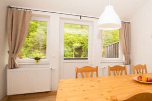 A dining area with a wooden table, four chairs, a hanging light fixture, and a view of greenery through the windows. - in the forester's lodge on the Brocken mountain - 3 bedrooms (Ilsenburg)