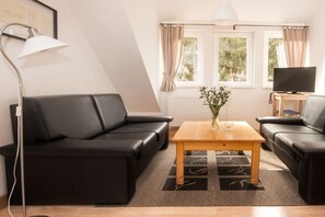 Ein modernes Wohnzimmer mit einem schwarzen Ledersofa, einem Holztisch, einer Stehlampe und einem Fernseher auf einem Holzschrank.