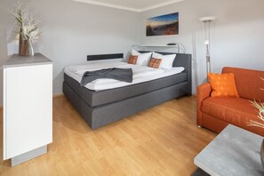 Ein modernes Schlafzimmer mit einem Bett, einer Couch, einem Schreibtisch und einem Gemälde an der Wand.