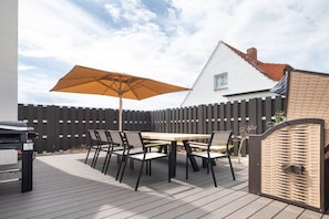 Eine Terrasse im Freien mit Tisch, Stühlen, einem Grill und einem großen Sonnenschirm.