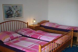 A room with two wooden beds, each with a pink and white quilt. There is a nightstand with a lamp between the beds. A painting hangs on the wall above the beds. - Holiday home with 7 bedrooms (Bad Sachsa)
