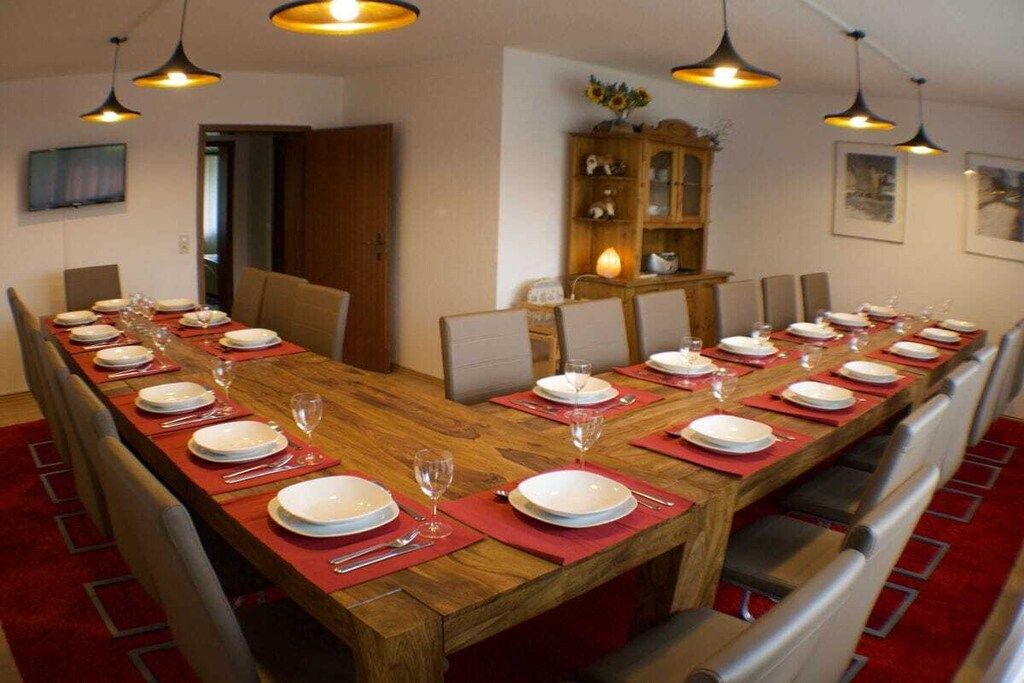 A dining room with a long wooden table set for a meal, surrounded by chairs, with pendant lights above.