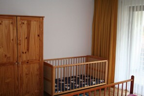 A wooden crib with a patterned mattress, a wooden wardrobe, and a window with curtains. - Holiday home with 7 bedrooms (Bad Sachsa)