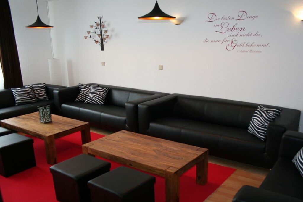 A modern living room with a black leather sofa, two wooden coffee tables, and black and white patterned cushions.