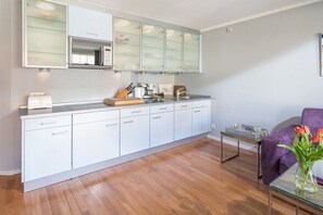 Una cocina moderna con armarios blancos, horno empotrado y una mesa de comedor de vidrio.