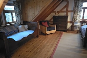 Ein Zimmer mit Holzboden, einem Bett mit weißer Bettdecke, einem Holzstuhl, einem Schminktisch und einem Fenster mit Vorhängen.