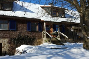 Une maison à deux étages avec une façade en briques, un escalier en bois menant à l’entrée et un toit recouvert de neige.