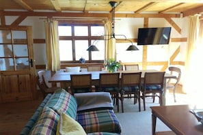 Ein gemütliches Zimmer mit einer Couch, einem Esstisch, Stühlen, einem Fernseher und einem fenster mit Vorhängen.