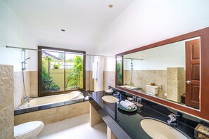 Ein Badezimmer mit einer Badewanne, zwei Waschbecken, einem großen Spiegel und Blick auf Grünflächen.
