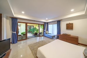 Quarto com uma cama grande, cômoda de madeira, televisão e porta de vidro corria para uma varanda.