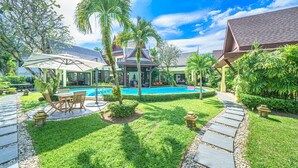Ein Poolbereich mit freiem Blick auf den Pool, umgeben von gepflegtem Rasen, Palmen und einem Pavillon.