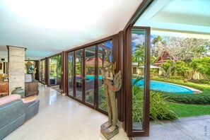 Ein großzügiger Innenbereich mit einer großen Glasdoor, die zu einem Schwimmbecken und üppiger Bepflanzung führt.