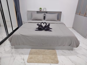 A modern bedroom with a large bed, a bedside table, a nightstand, a window with curtains, and a small potted plant.