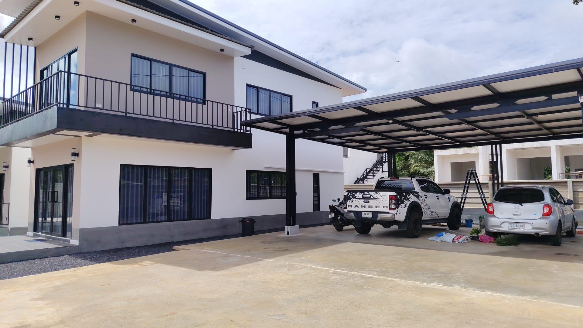 A two-story building with a covered parking area, a white pickup truck, and a silver car parked outside.