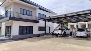 A two-story building with a covered parking area, a white pickup truck, and a silver car parked outside. - Charming Lodge With Mountain Views in Mu (Krabi)