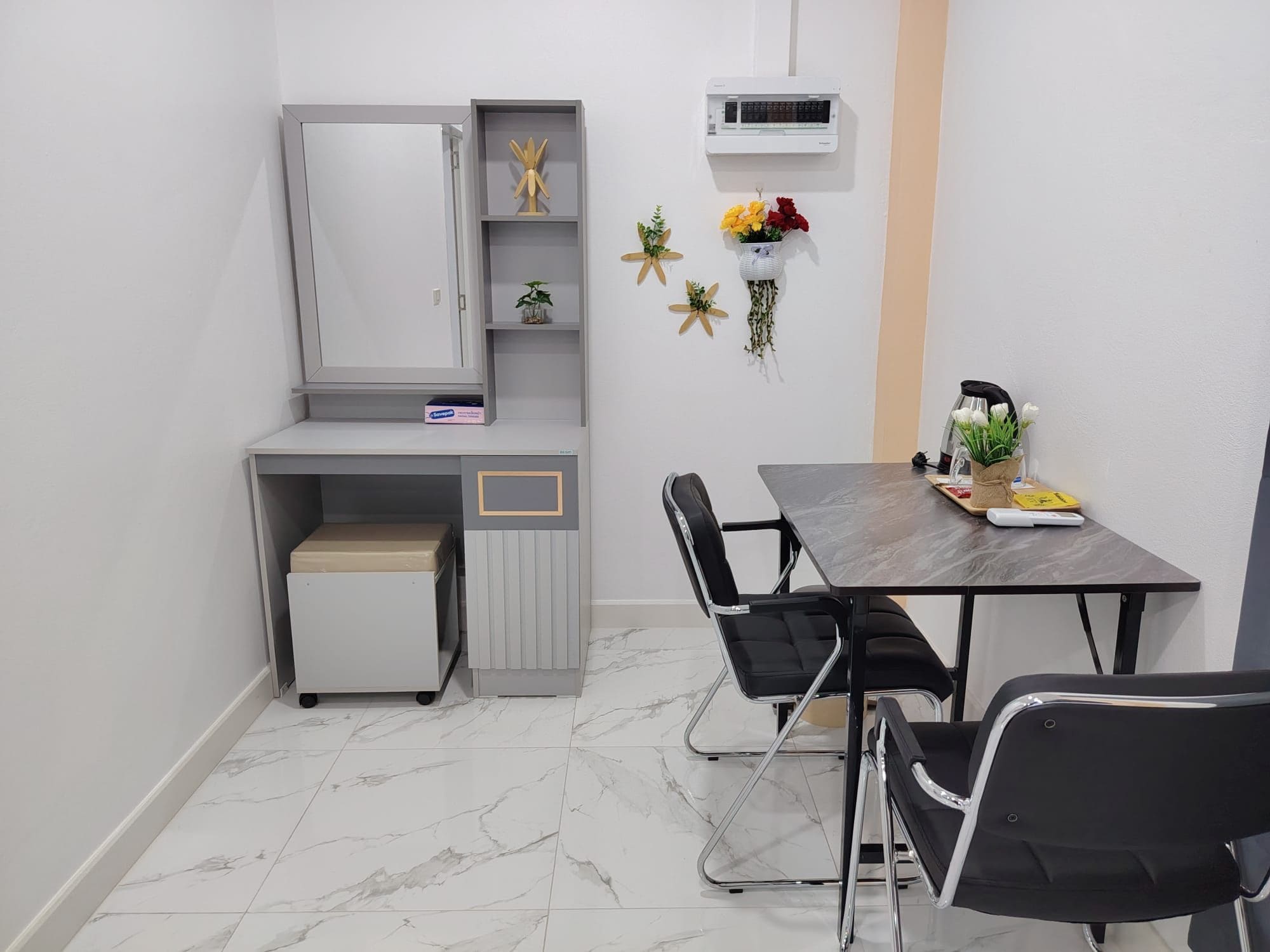 A small, modern room with a grey cabinet, a small table with chairs, a heater, and a wall-mounted air conditioner.