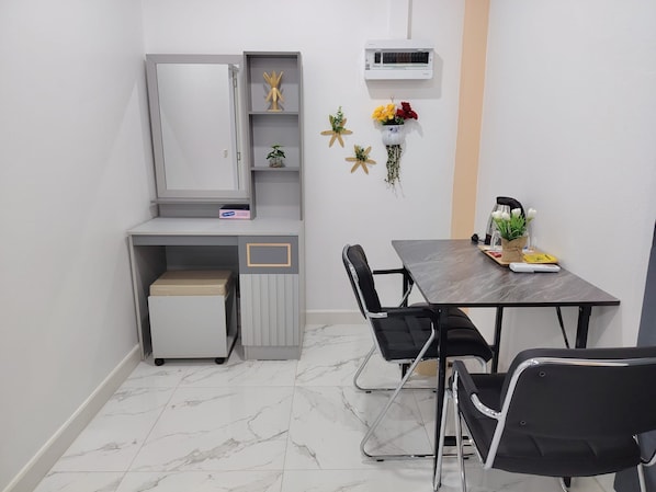 A small, modern room with a grey cabinet, a small table with chairs, a heater, and a wall-mounted air conditioner.