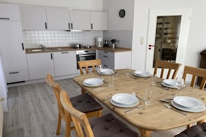 Eine moderne Küche mit weißen Schränken, einem Holzespeisetisch für sechs Personen und einer sichtbaren Uhr an der Wand.