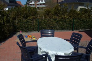 Eine Terrassengruppe mit Tisch und Stühlen, umgeben von einer Hecke und Gebäuden im Hintergrund.