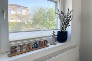 A window sill with a wooden sign spelling 'STRAND,' a potted plant, and a small decorative item. - Holiday home with 3 bedrooms (Timmendorfer Strand)