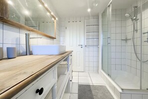 A modern bathroom with a wooden vanity, a large mirror, a white sink, and a glass shower enclosure. - Holiday home with 3 bedrooms (Timmendorfer Strand)