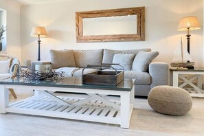 Un salon comprenant un canapé, une table basse en verre, deux lampadaires et un miroir décoratif accroché au mur.