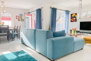 A modern living room with a light blue sofa, a dining table with chairs, and a TV. - Holiday home with 2 bedrooms (Timmendorfer Strand)