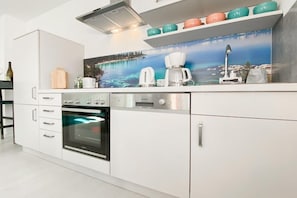 A modern kitchen with a built-in oven, a coffee maker, and a decorative backsplash. - Holiday home with 2 bedrooms (Timmendorfer Strand)