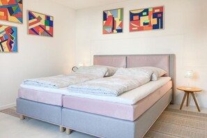 A bedroom with a bed, pillows, a bedside table, and abstract wall art. - Holiday home with 2 bedrooms (Timmendorfer Strand)