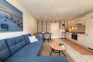 A modern living room with a sofa, a coffee table, and a dining area with chairs. - Holiday apartment with 1 bedroom (Travemünde)