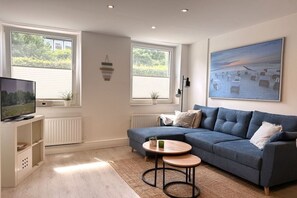 A living room with a sofa, a coffee table, a television, and a painting on the wall. - Holiday apartment with 1 bedroom (Travemünde)