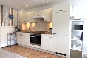 Una cocina moderna con armarios blancos, horno empotrado y protector de salpicadero de madera.
