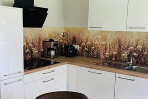 A kitchen with white cabinets, a coffee maker, and a kettle on the countertop. - Holiday apartment in Nesse with swimming pool (Nesse)