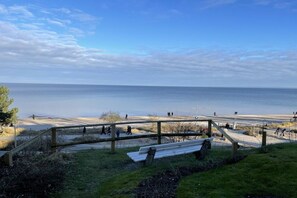 Une promenade en bord de mer, agrémentée de bancs et d’une rambarde en bois, qui mène à la mer.