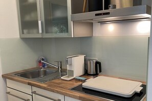 Une cuisine moderne équipée d’un évier en acier inoxydable, d’une machine à café, d’une bouilloire et d’une planche à découper posée sur le plan de travail.