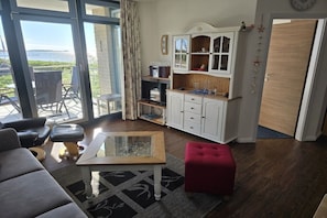 A living room with a glass coffee table, a red ottoman, a white cabinet, and a view of the outdoors. - Sea view South Beach Sü 028 (Burg-Tiefe)