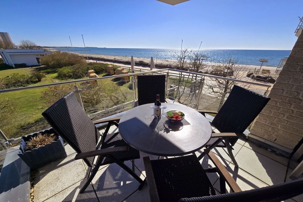 Varanda com mesa e cadeiras, com vista para a praia e o oceano.