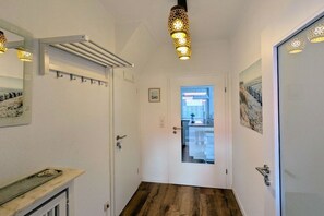 A hallway with a coat rack, a door leading to a kitchen, and a hanging light fixture. - Holiday home in Borkum with swimming pool (Borkum)