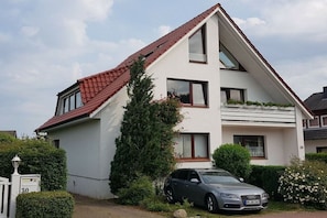 A two-story residential building with a sloped roof, a car parked in the driveway, and a mailbox with the number 30. - Holiday apartment with 2 bedrooms (Scharbeutz)