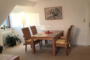 A dining area with a table and chairs, a radiator, a potted plant, and a painting on the wall. - Holiday apartment with 2 bedrooms (Scharbeutz)