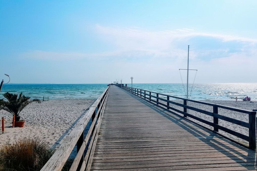 A wooden pier leading to a sandy beach with a clear sky.