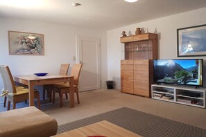 A living room with a dining table, chairs, a television, a cabinet with glassware, and a framed picture on the wall. - Holiday apartment with 2 bedrooms (Scharbeutz)