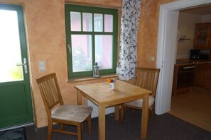 A room with a wooden table and chairs, a window with green shutters, and a view of a kitchen. - Baltic Sea House Sea Wonders (Born)