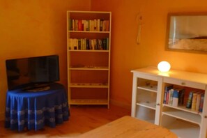 Una habitación con televisión, una estantería y una mesa.