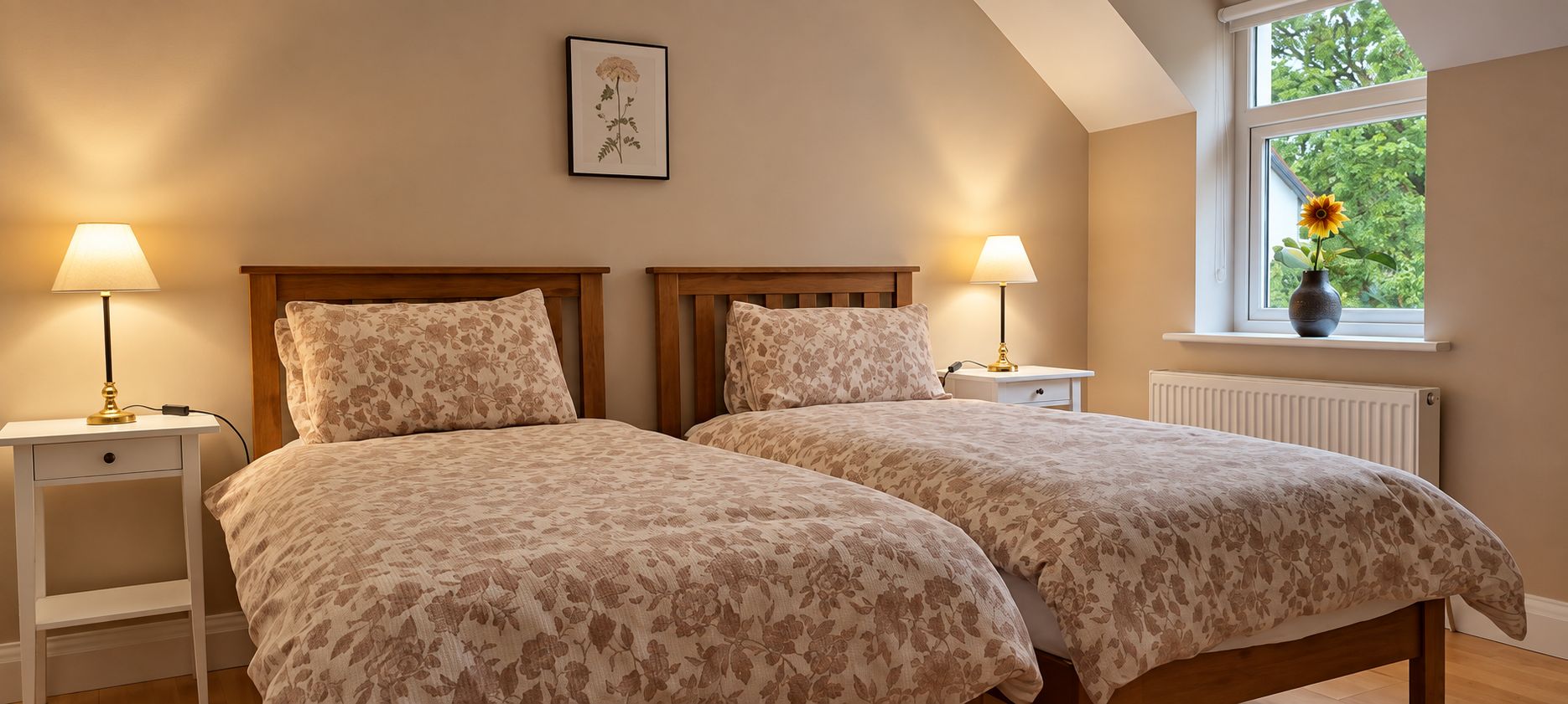 Une chambre avec deux lits, des lampes de chevet, un tableau encadré au mur et une fenêtre donnant sur un paysage verdoyant.