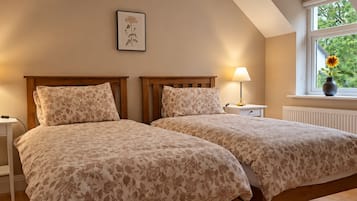 Une chambre avec deux lits, des lampes de chevet, un tableau encadré au mur et une fenêtre donnant sur un paysage verdoyant.