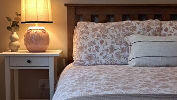 A bedroom with a bed, a nightstand with a lamp, a vase with a plant, and a framed picture on the wall.