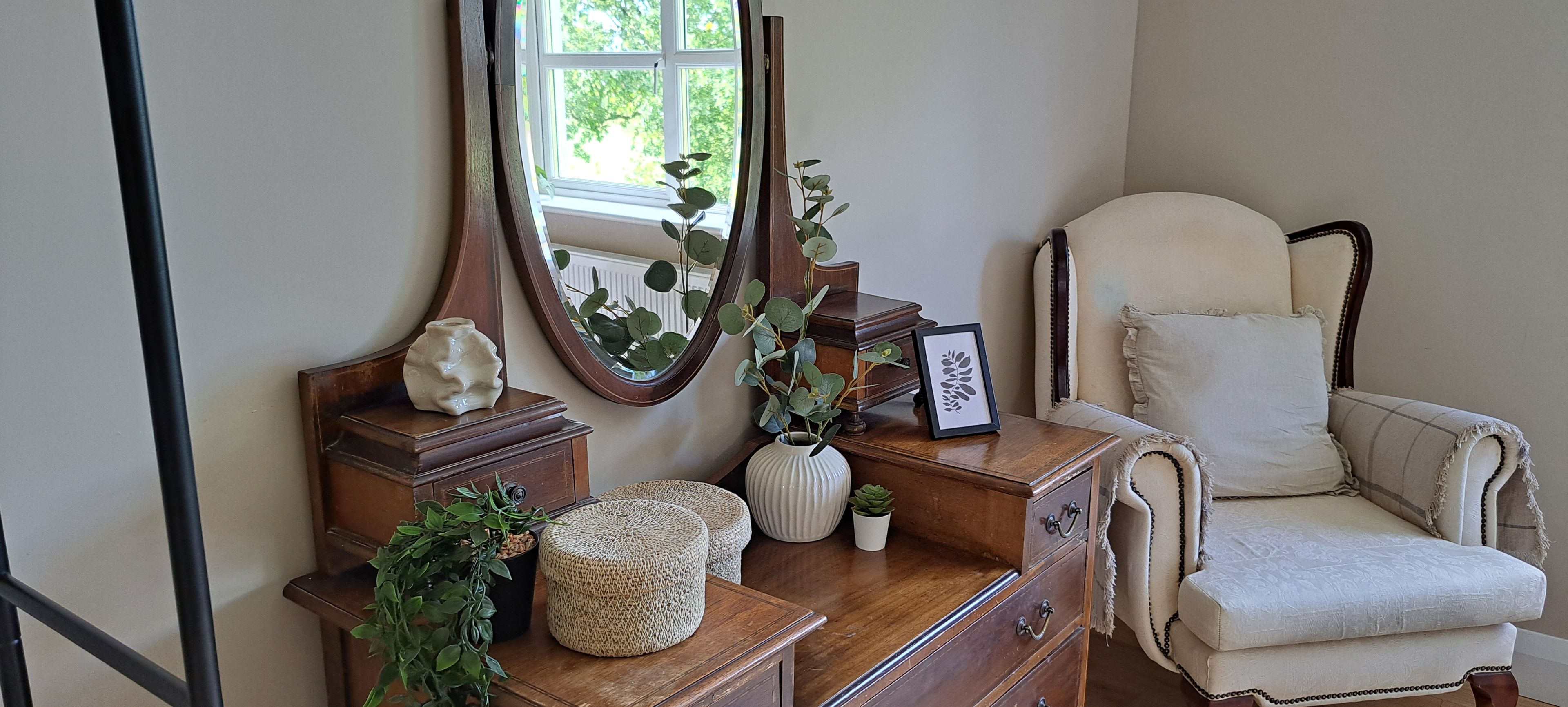 A room with a wooden dresser, a mirror, a framed picture, a white chair, and a potted plant.