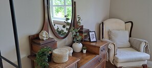 A room with a wooden dresser, a mirror, a framed picture, a white chair, and a potted plant.
