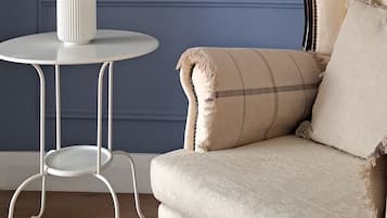A room with a blue wall, a framed artwork, a white table with a vase of flowers, and a beige sofa.